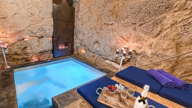 Zona de spa con paredes de piedra, una bañera de hidromasaje, velas y una bandeja con champán y fresas.