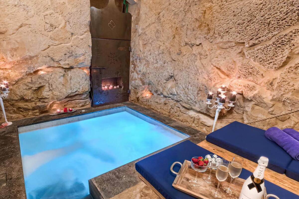 A stone-walled spa area with a hot tub, candles, and a tray with champagne and strawberries.