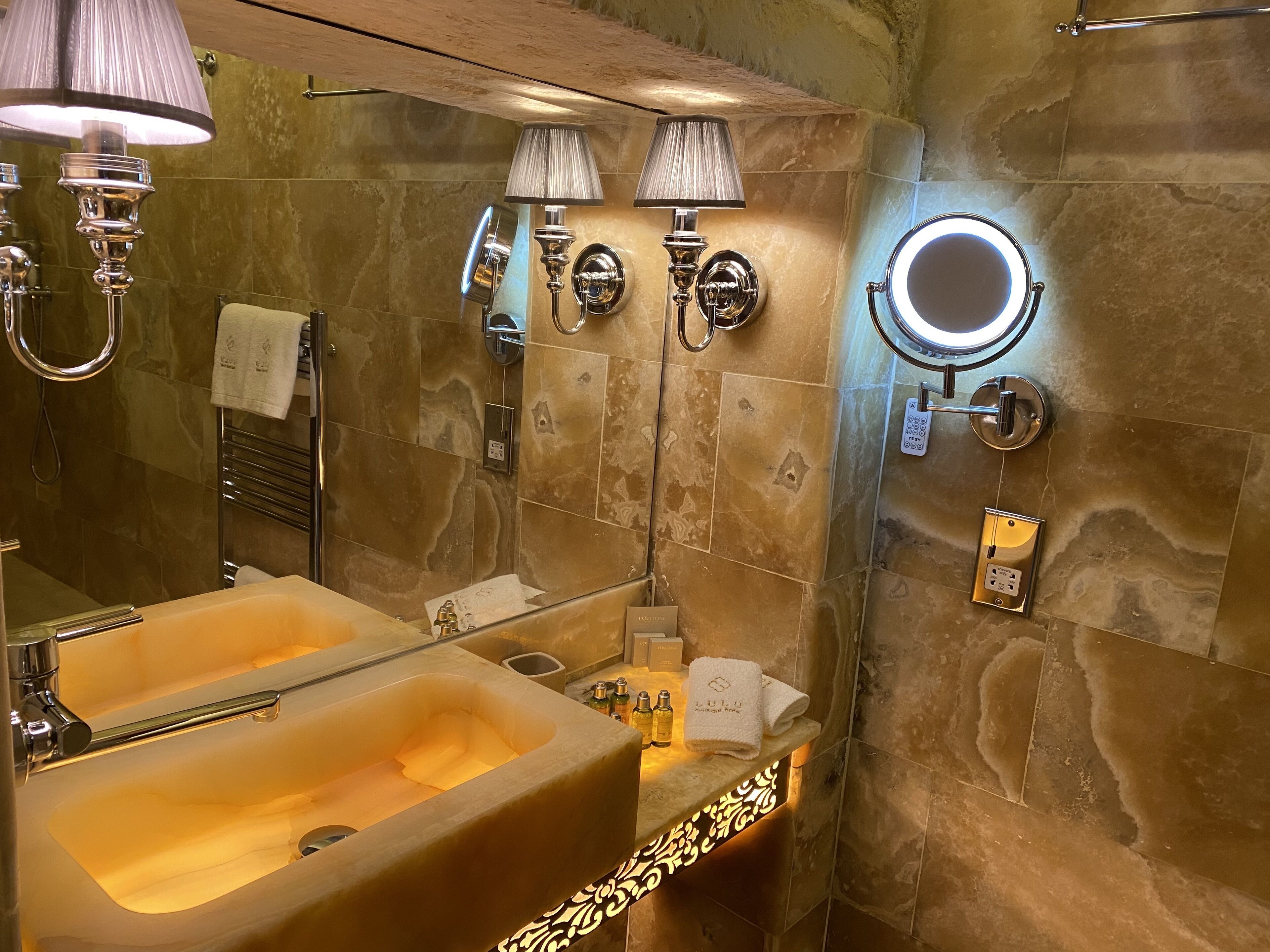Baño con lavamanos doble, espejo de tocador, toallero e iluminación en la pared.