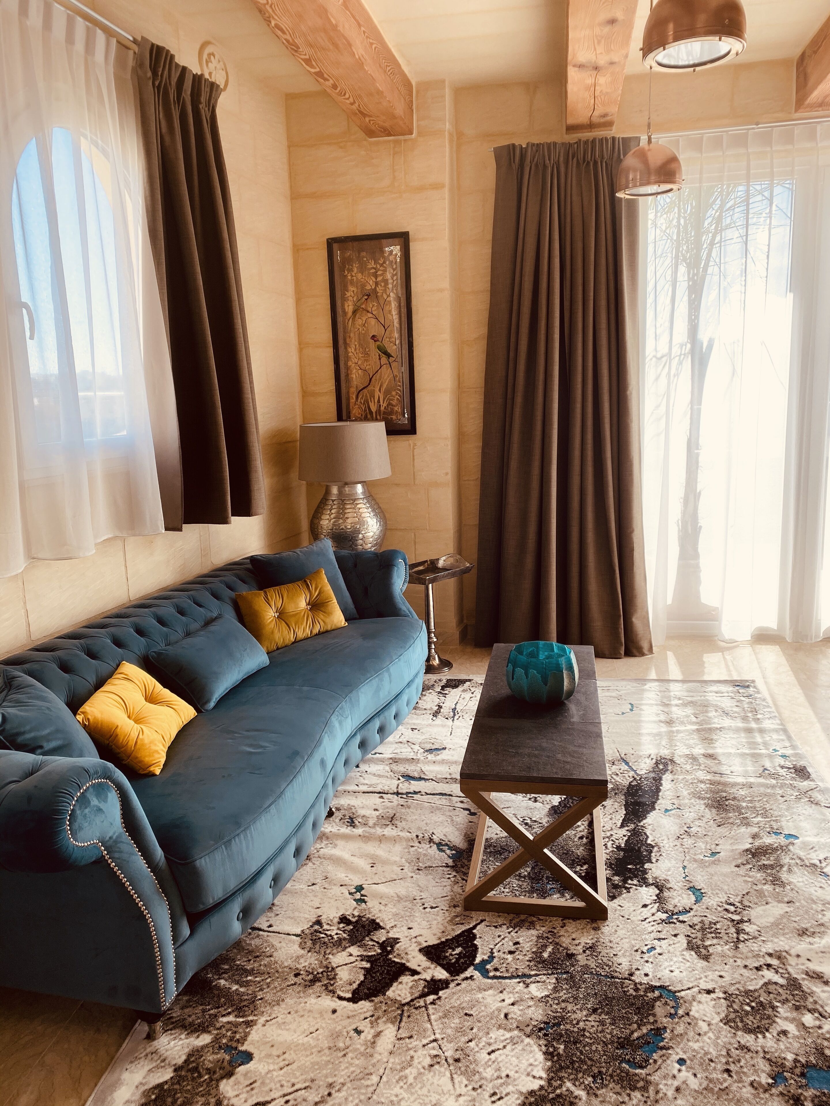 A living room with a blue sofa, a patterned rug, and a table with a blue bowl.