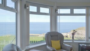 A room with a view of the sea, a grey armchair with a yellow pillow, and a small wooden table. - Seabreezes - UK30690 (Portknockie)