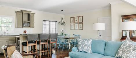 A spacious living room with a blue sofa, a wooden coffee table, and a dining area with a chandelier.