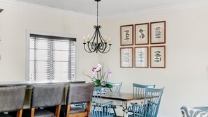 Un coin repas avec une table et des chaises en bois, un lustre et des illustrations de poissons encadrées au mur.