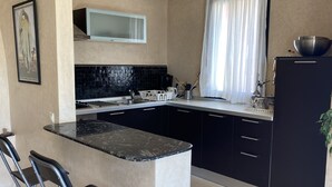 A compact kitchen with a black countertop, a microwave, and a sink. There are two black chairs and a potted plant. - lights in Mogador, the charm of essaouira and the attraction of the seaside! A few meters away you are already on the beach. You can discover its many souks and explore its surroundings easily.   (essaouira)