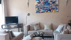 A living room with a sofa, armchairs, a coffee table, a TV, and a painting on the wall. - lights in Mogador, the charm of essaouira and the attraction of the seaside! A few meters away you are already on the beach. You can discover its many souks and explore its surroundings easily.   (essaouira)