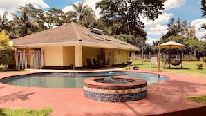 Piscina com hidromassagem, rodeada por um terraço de tijolos e uma área coberta com mobiliário de exterior.