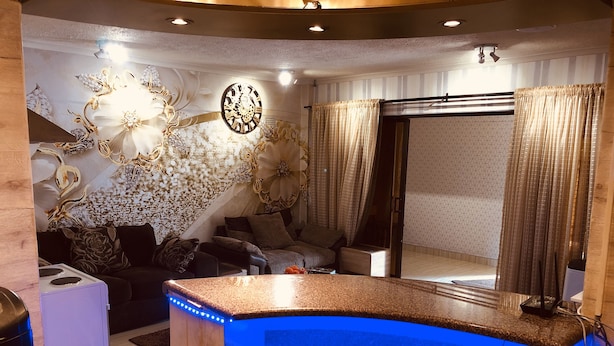 Uma sala de estar moderna com uma mesa de bilhar iluminada em azul, um relógio de parede decorativo e um espaço de estar aconchegante.