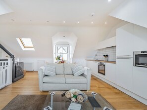 Un appartement moderne de style « loft », avec un plafond haut, un canapé gris, une cuisine dotée de meubles blancs et une lucarne.