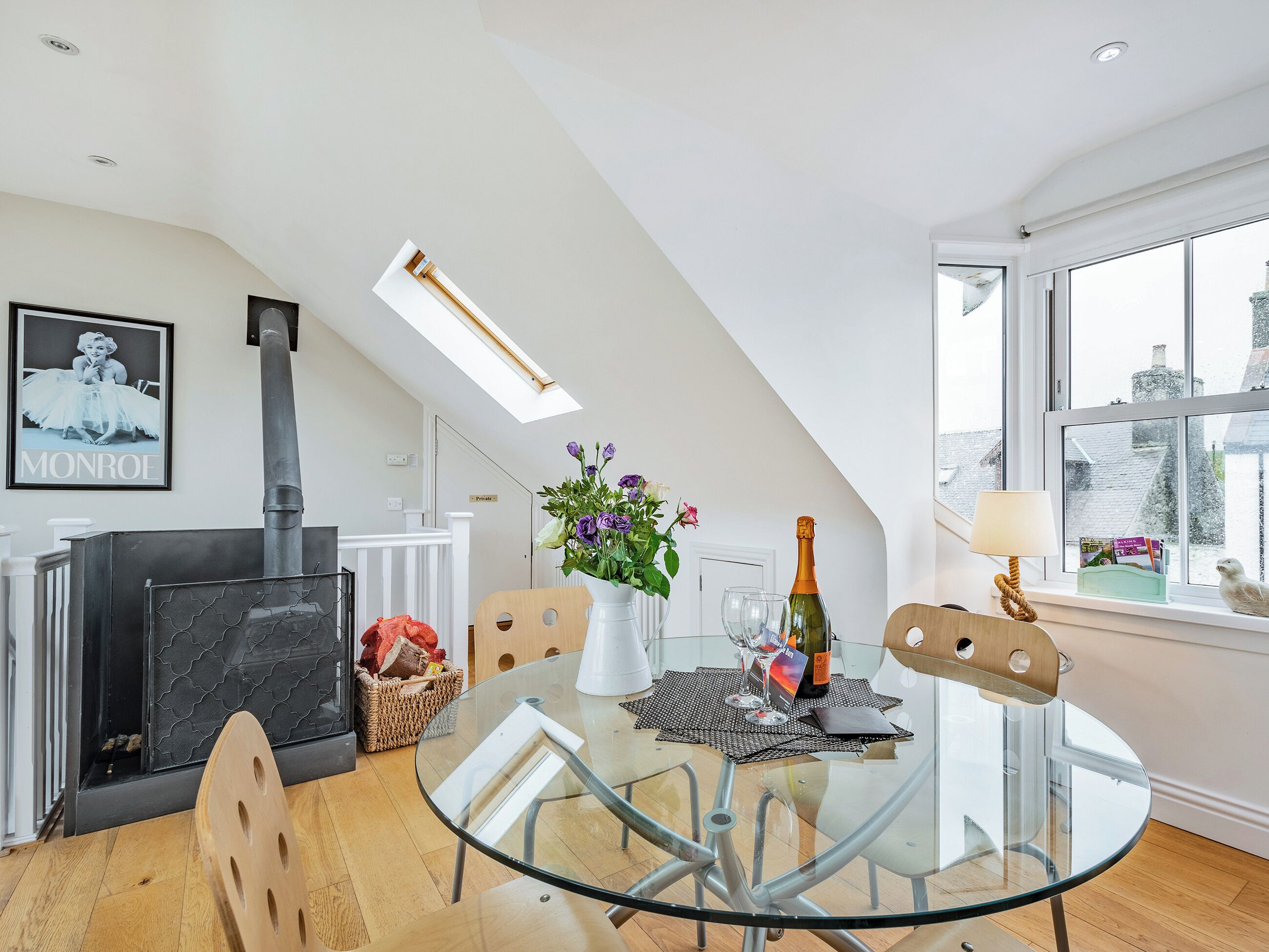 A modern interior with a glass dining table, a fireplace, and a view through a large window.