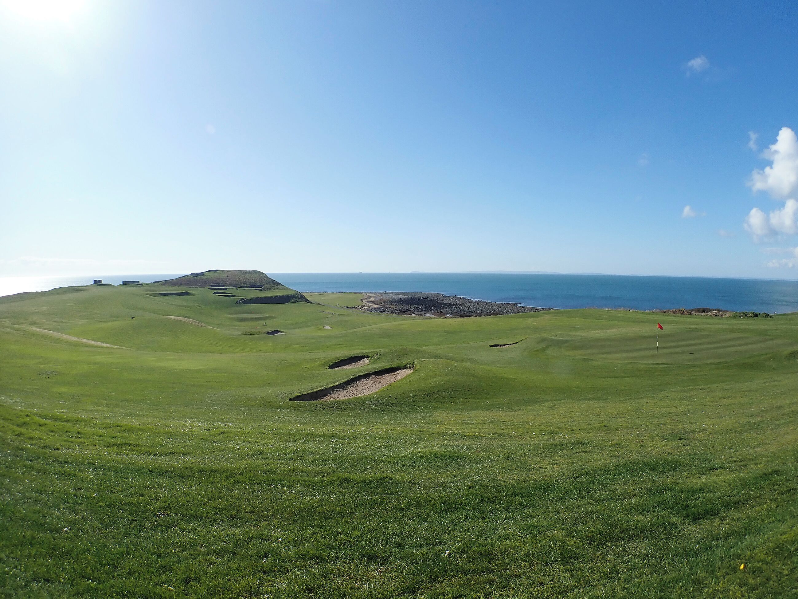 A golf course with a coastal view, bunkers, and a flagstick.