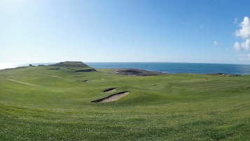 A golf course with a coastal view, bunkers, and a flagstick.