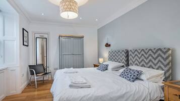 A bedroom with a bed, bedside tables, a wardrobe, a chair, and a hanging light fixture.