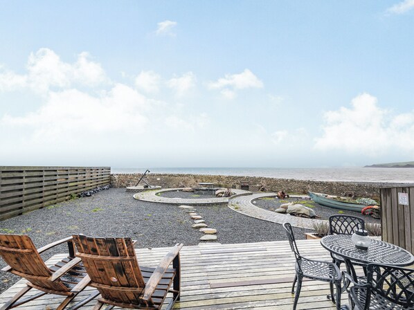 Eine Holzterrasse mit Sitzgelegenheiten im Freien, ein geschwungener Weg und Blick aufs Meer.