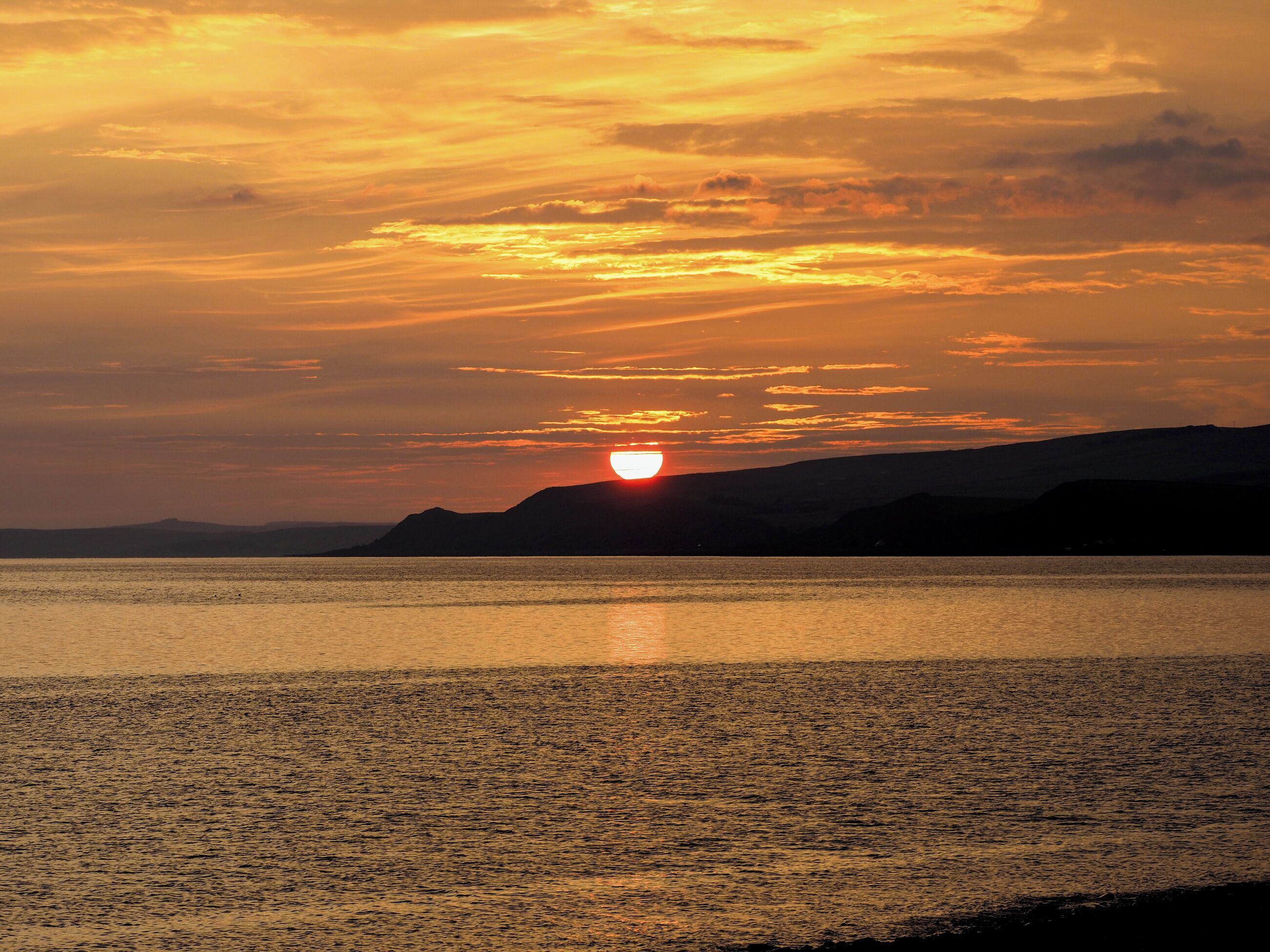 Solnedgang over et roligt vandareal med fjerne landskaber.