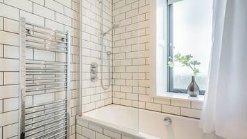 A bathroom with white tiled walls, a shower with a glass door, a window with a plant, and a towel rack.