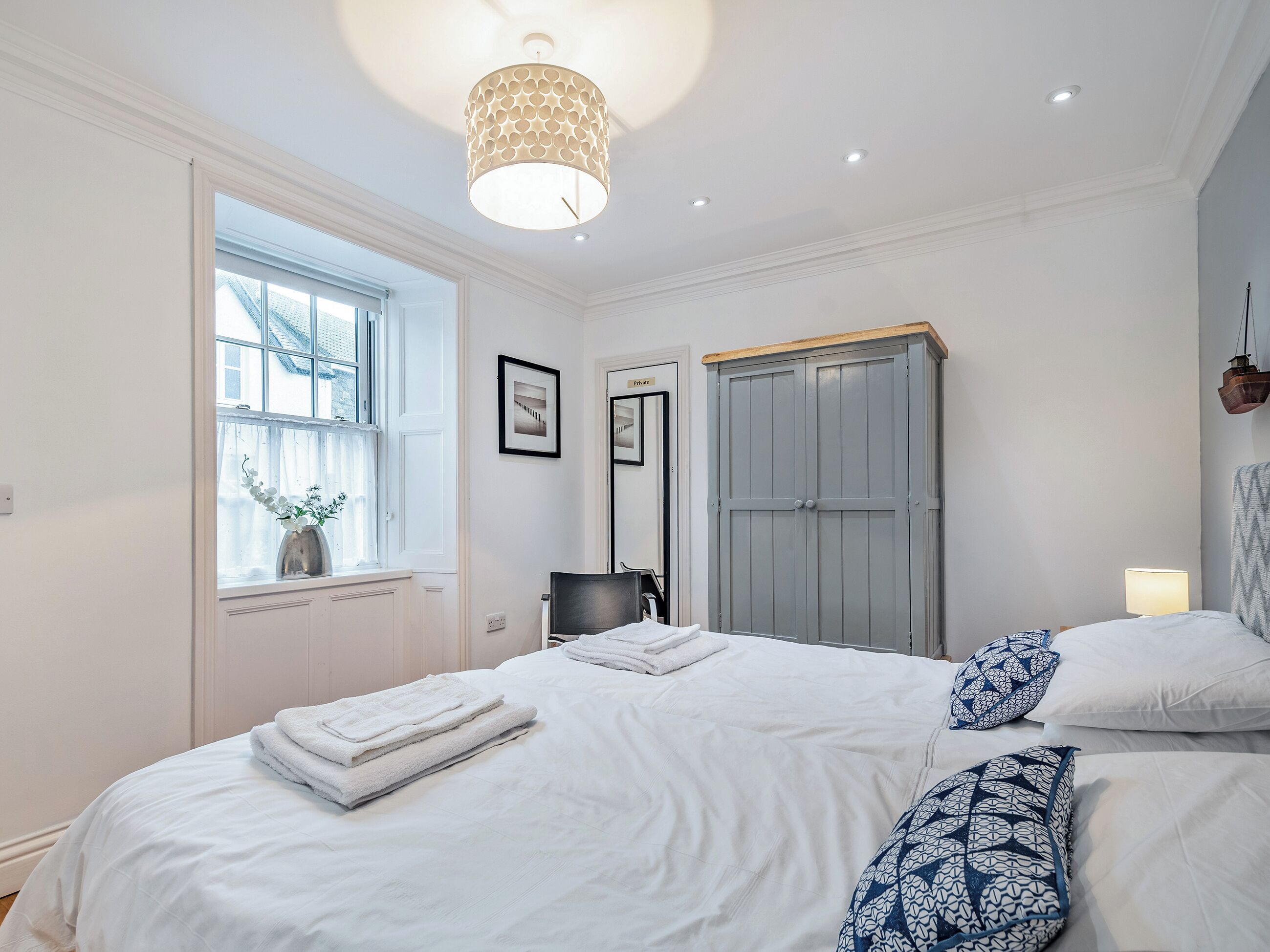 Un dormitorio con cama, armario, ventana y lámpara colgante.