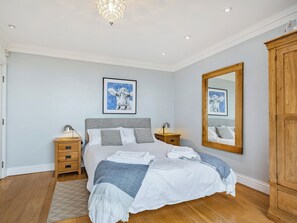 Une chambre à coucher avec un lit, des tables de chevet, un miroir et une armoire.