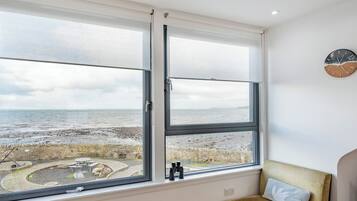 A room with a large window overlooking a beach, a clock on the wall, and a cushioned bench.