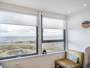 A room with a large window overlooking a beach, a clock on the wall, and a cushioned bench. - 2 bedroom accommodation in Port William (Port William)