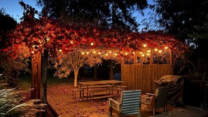 Relax in a serene outdoor space surrounded by trees, with a pergola, benches, and tables perfect for dining or unwinding.