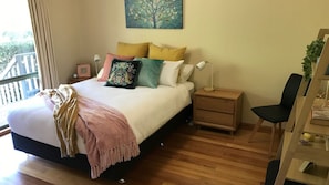 Een slaapkamer met een bed, nachtkastjes, een stoel, een schilderij en uitzicht op een balkon.
