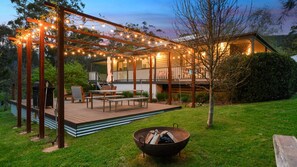 Eine Terrasse mit Gartenmöbeln, einem Feuerkorb und Lichterketten.