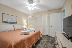 Une chambre à coucher avec un lit, un ventilateur de plafond, un tableau, une lampe, un téléviseur et une armoire.