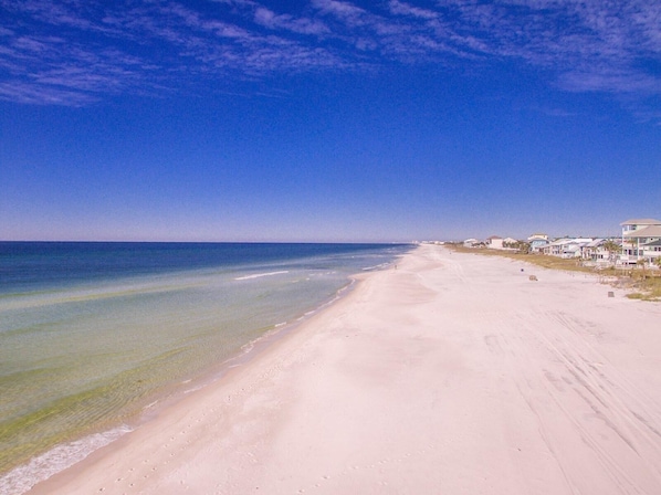 Une plage aux eaux cristallines, un rivage sablonneux et des bâtiments qui bordent la côte.