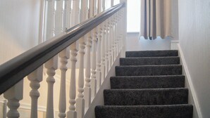 A staircase with white balusters and a dark handrail, leading to a room with a window and curtains. - 2 bedroom accommodation in Amble, near Warkworth (Amble, near Warkworth)