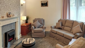 A living room with a fireplace, a sofa, a chair, and a round ottoman. - 2 bedroom accommodation in Amble, near Warkworth (Amble, near Warkworth)