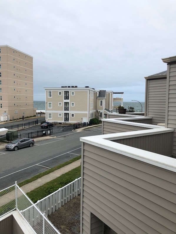 A coastal residential area with a road, a parking lot, and buildings with balconies overlooking the sea.