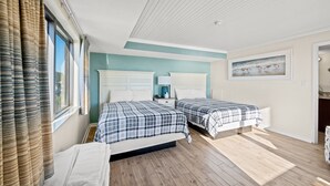 A bedroom with two beds, a window with curtains, a painting on the wall, and a wooden floor.