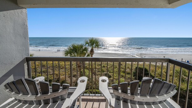 A balcony with two Adirondack chairs facing a beach.