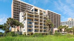 A multi-story hotel with balconies, surrounded by palm trees and greenery.