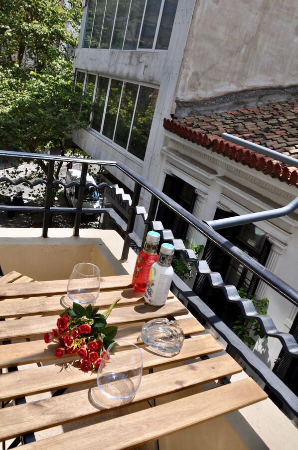 A wooden table with a bouquet of red roses, two wine glasses, and two bottles of water on a balcony with a metal railing. - Athens Historic Centre Renovated Apartment (Athina)