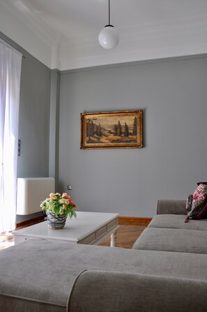 A living room with a grey sofa, a white coffee table, a framed painting, and a vase with flowers. - Athens Historic Centre Renovated Apartment (Athina)
