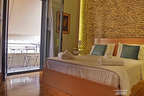 Relax in this stylish room with a large bed, a small table, and a chair near the window, offering a view of the outside balcony.