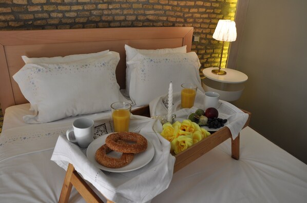 A neatly made bed with white linens, a tray with breakfast items including donuts, juice, and fruit, and a bedside lamp.