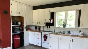 A kitchen with white cabinets, a gas stove, a microwave, and a red trash bin.