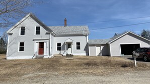 A two-story white house with a red door, a chimney, and a garage.