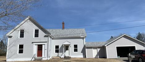 A two-story white house with a red door, a chimney, and a garage.