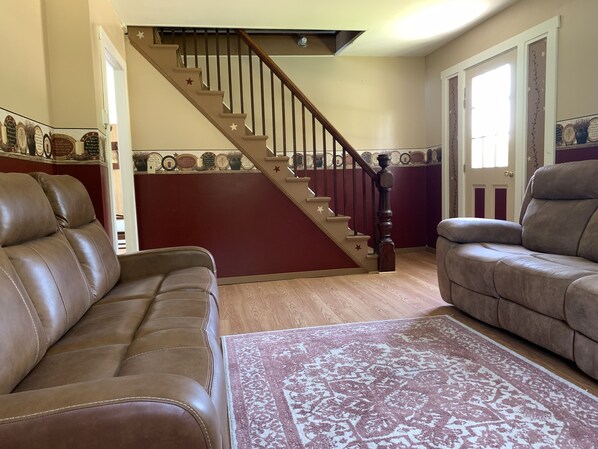 A living room with two brown leather sofas, a wooden staircase with star decorations, and a patterned rug.