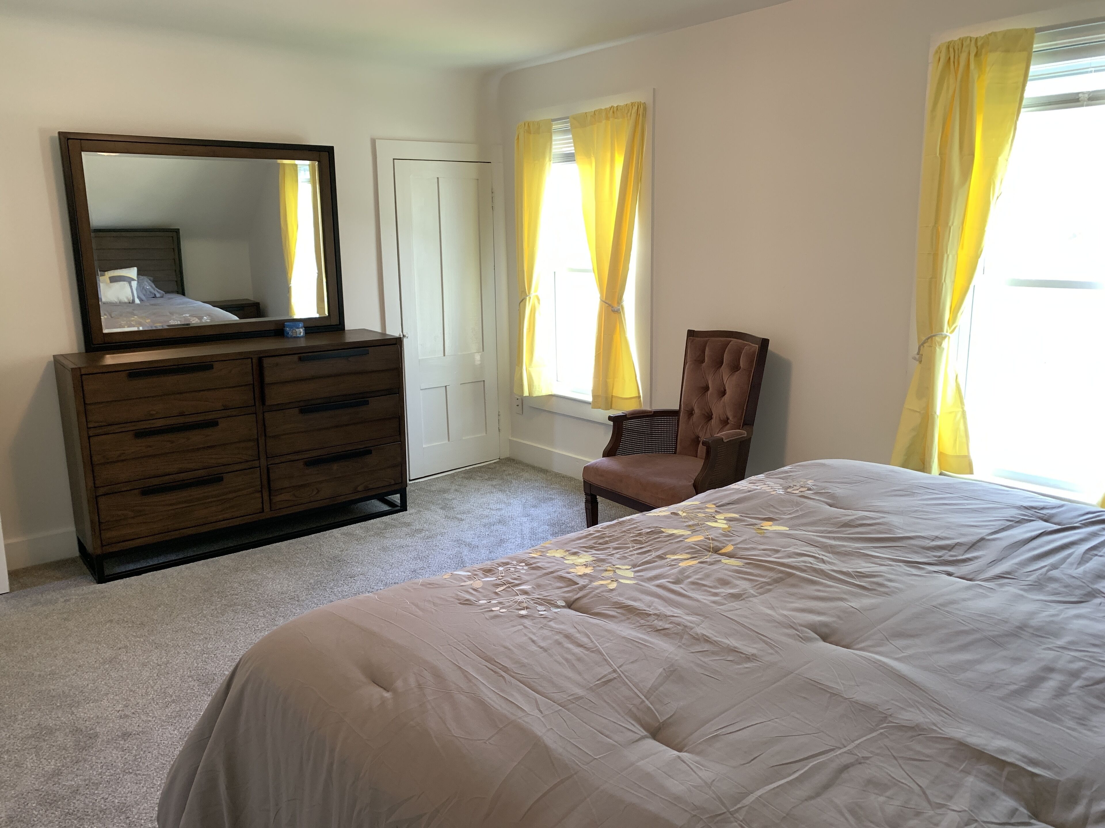 A bedroom with a bed, a dresser, a chair, and a window with curtains.