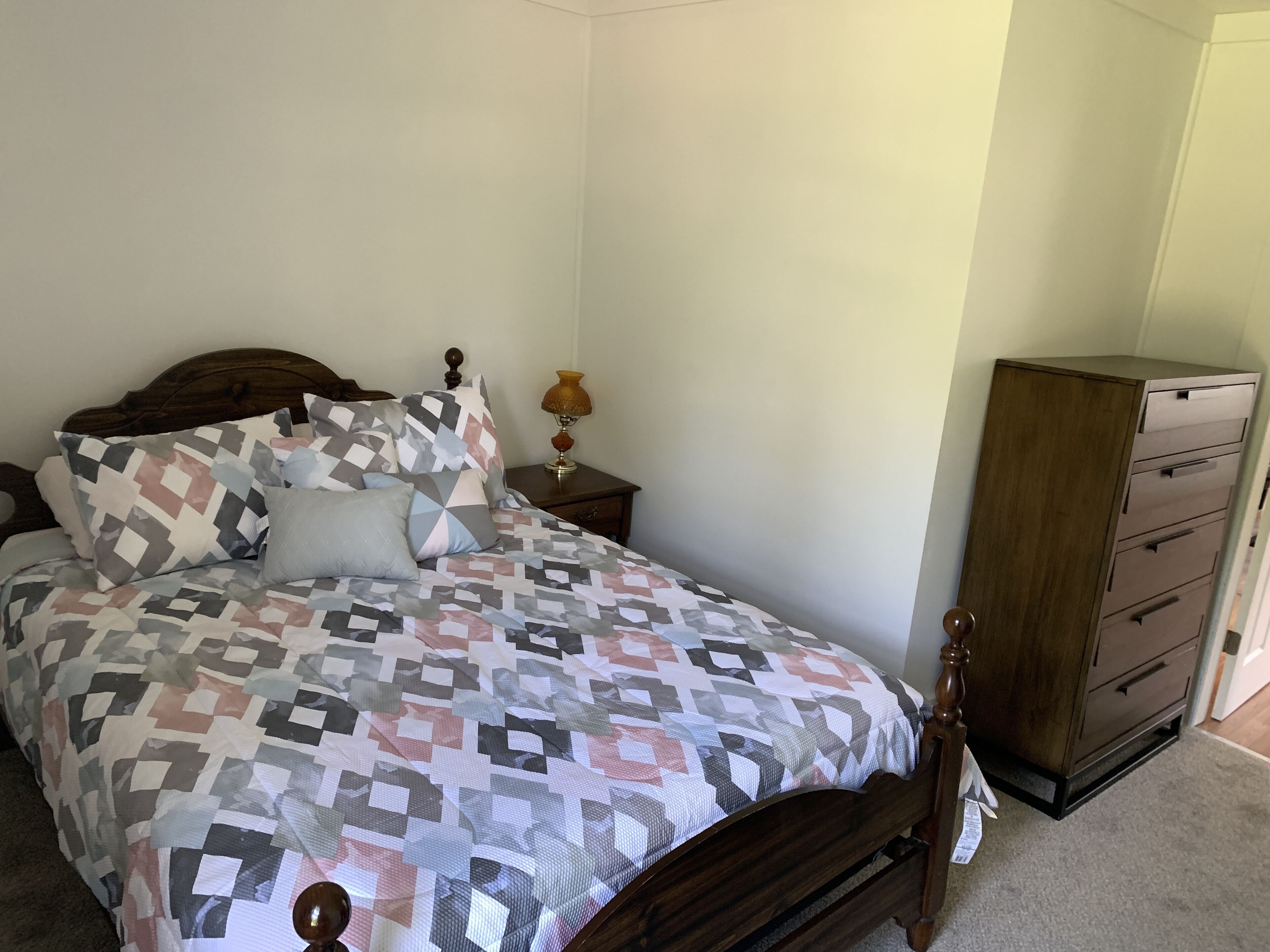 A bedroom with a bed, a nightstand, a lamp, and a dresser.