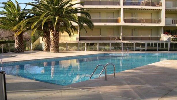 Ein Pool mit einer Metallleiter, umgeben von Palmen und einem mehrstöckigen Gebäude mit Balkonen.