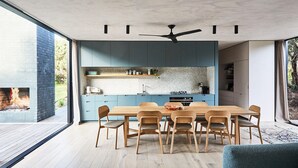 A modern kitchen with blue cabinets, a wooden dining table, and a ceiling fan. - THE BACH - ST ANDREWS BEACH (St Andrews Beach)