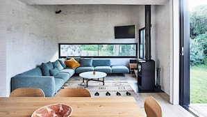A modern living room with a sectional sofa, a coffee table, and a dining area with chairs. - THE BACH - ST ANDREWS BEACH (St Andrews Beach)