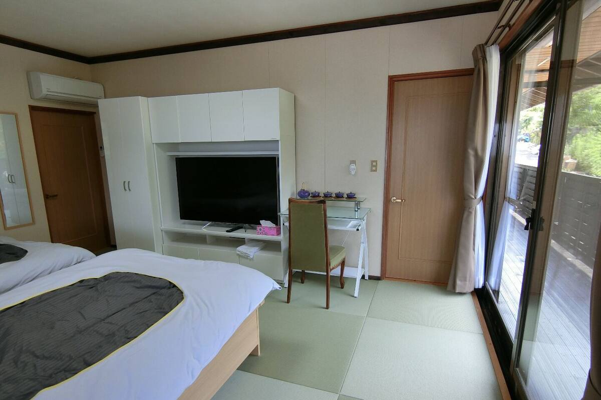 Une chambre d’hôtel comprenant un lit, un bureau avec une télévision, une chaise et une porte coulissante donnant sur un balcon.