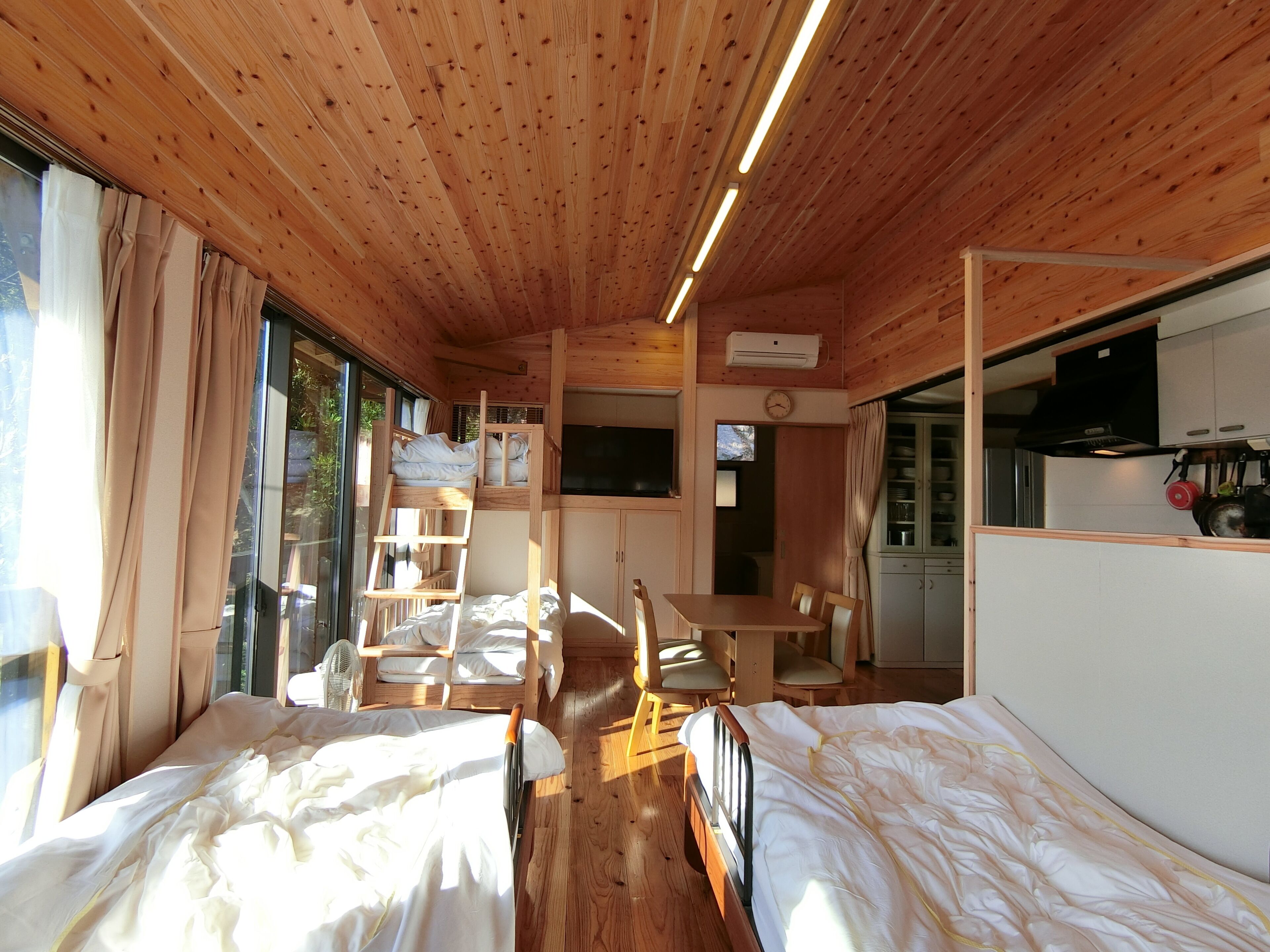 Una cabaña con dos camas, una mesa de comedor, una zona de cocina y un ventanal grande.