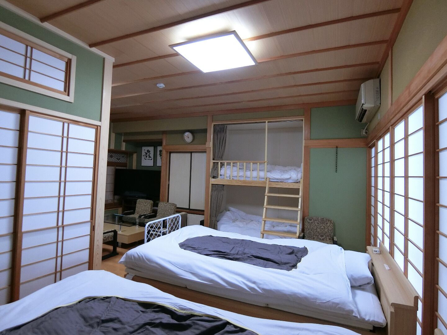 Una habitación con literas, un escritorio, una silla, un televisor y un reloj.